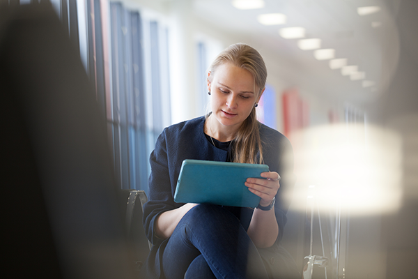 Woman waiting for F&I at auto dealership uses tablet to browse warranty, maintenance, and service information. 