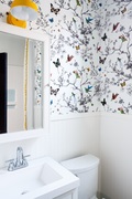 In this bathroom design, Bethany Adams uses the yellow light over the mirror and yellow trim on the shower curtain to ground the busy wallpaper featuring butterflies and birds. 